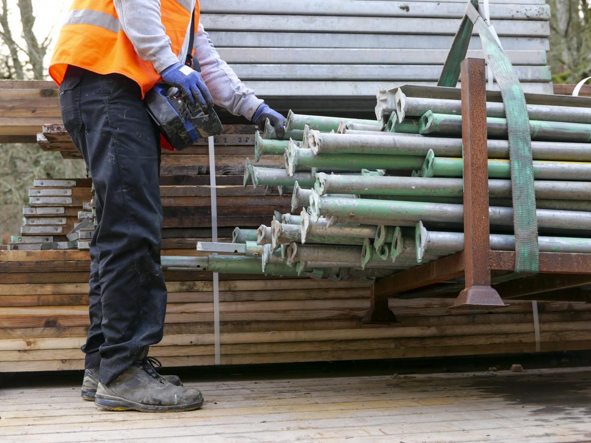 Man next to pile of unbuilt scaffolding beams